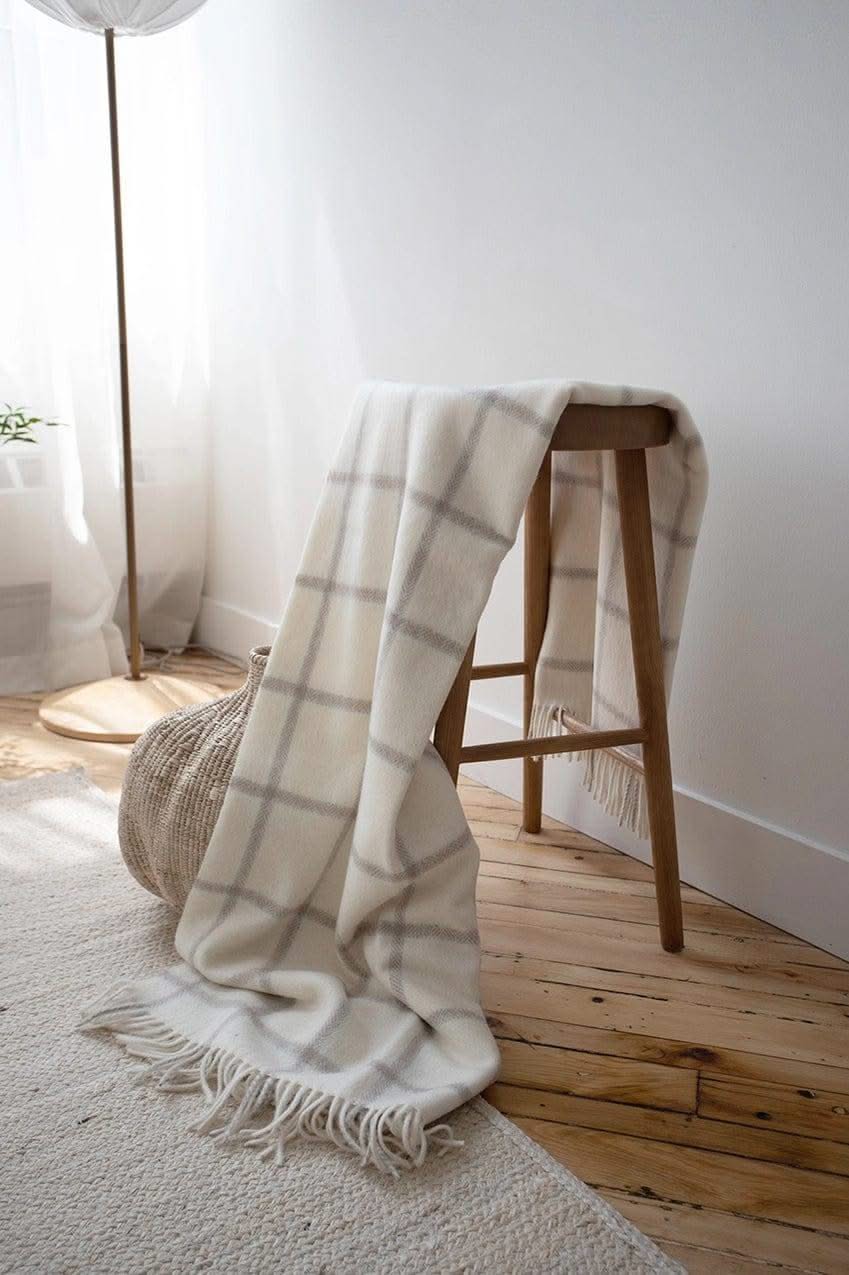 Picton Throw draped over a wooden stool in a cozy, light-filled room, emphasizing its classic check pattern and luxurious feel.