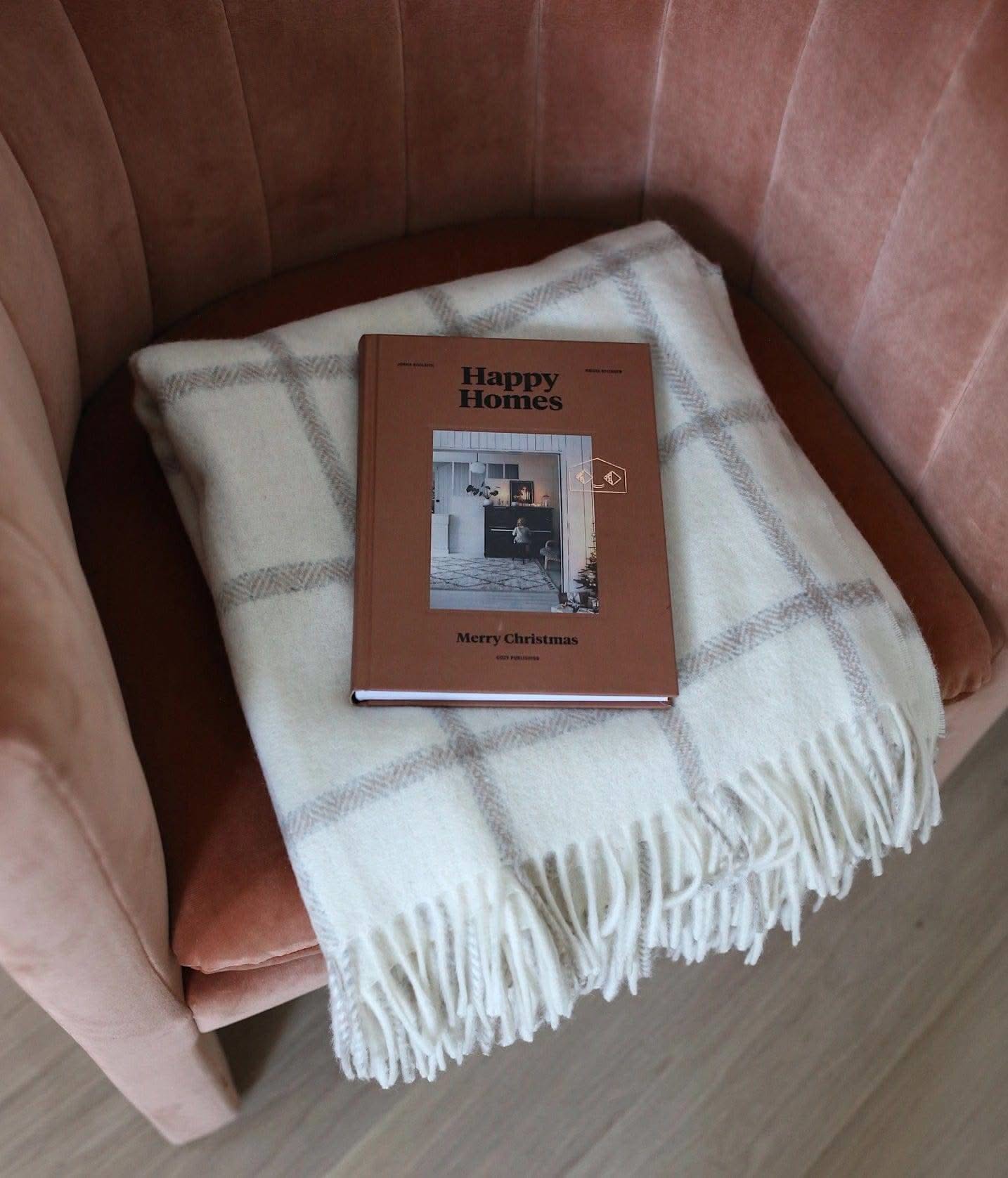 Picton Throw styled on a pink chair with a book, showcasing its off-white and light grey check pattern and fringed edges.