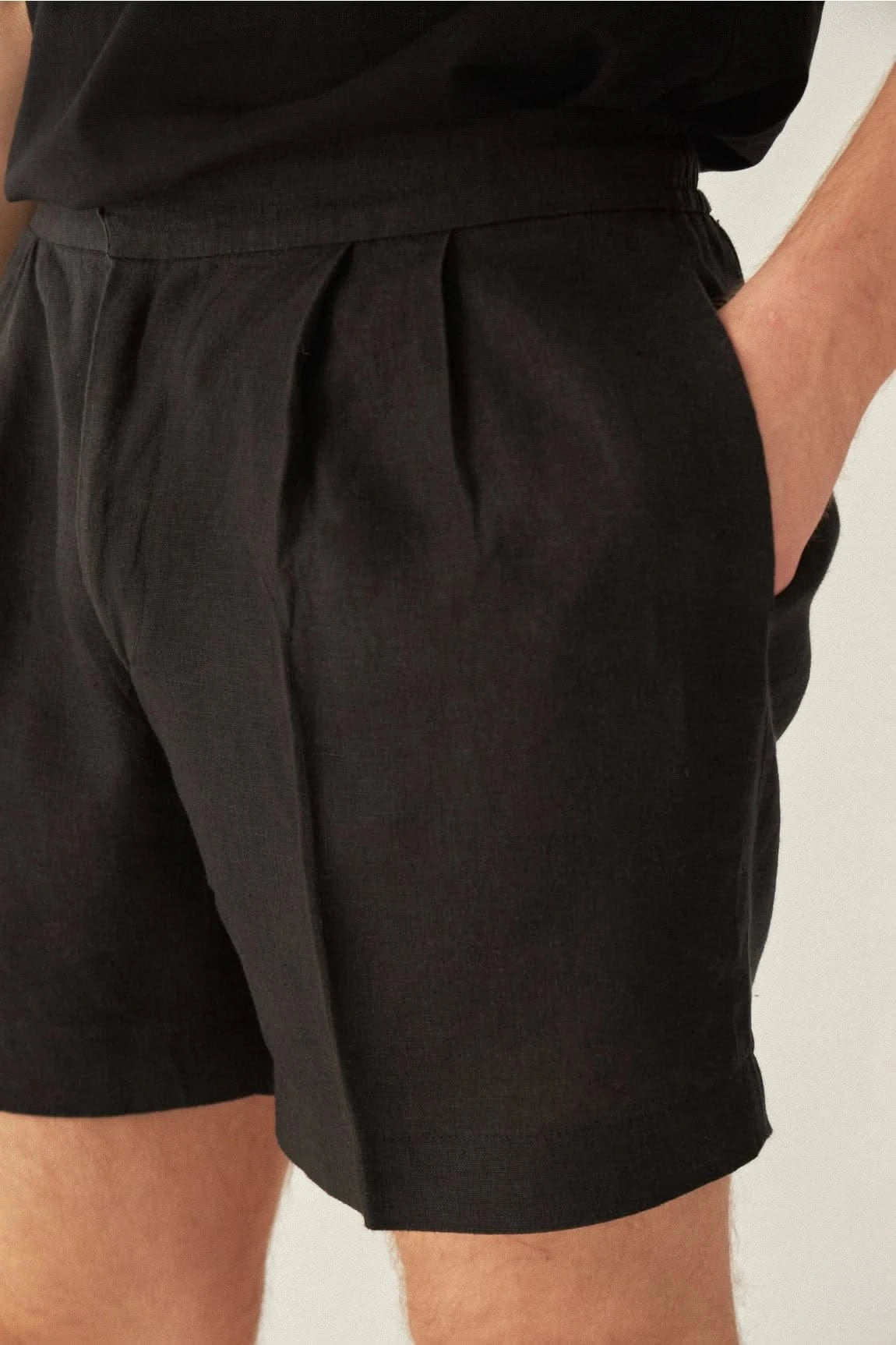 Close-up of mens black linen shorts pocket and pleats, showing fine stitching and breathable fabric for comfort and elegance.