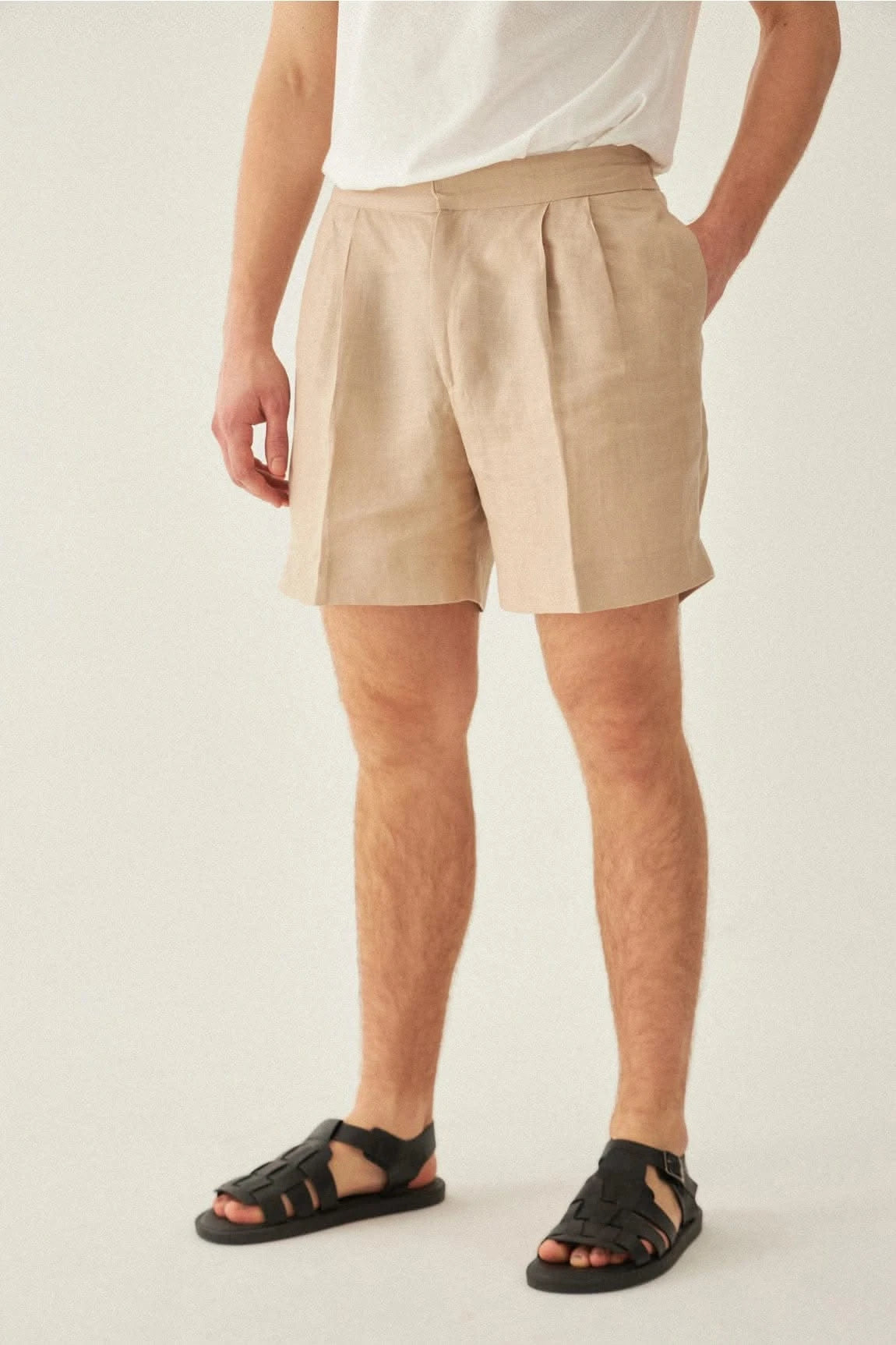Close-up of men's beige linen shorts paired with sandals, highlighting pleated front and side pockets for functional summer style.