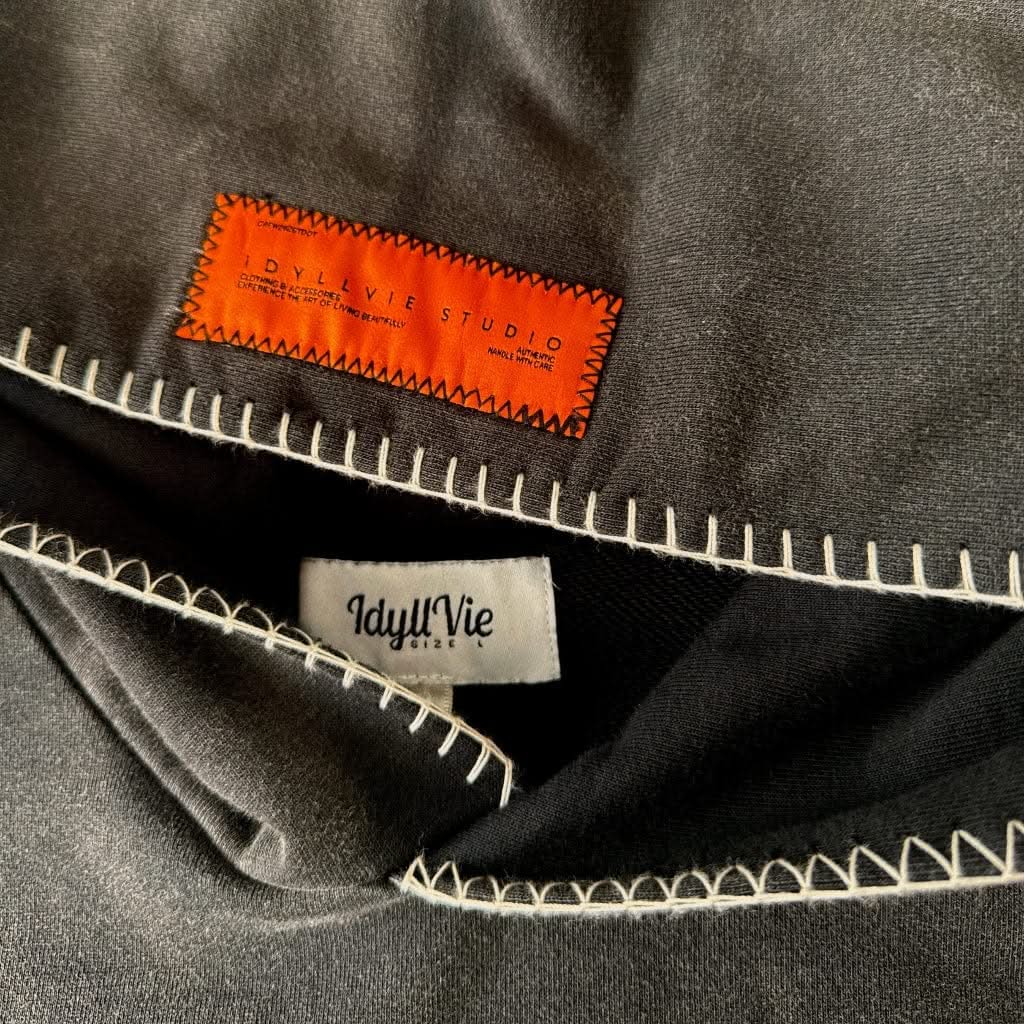 Close-up of IdyllVie Charcoal Hoodie neckline with visible contrast stitching and branded tags for premium apparel detailing.