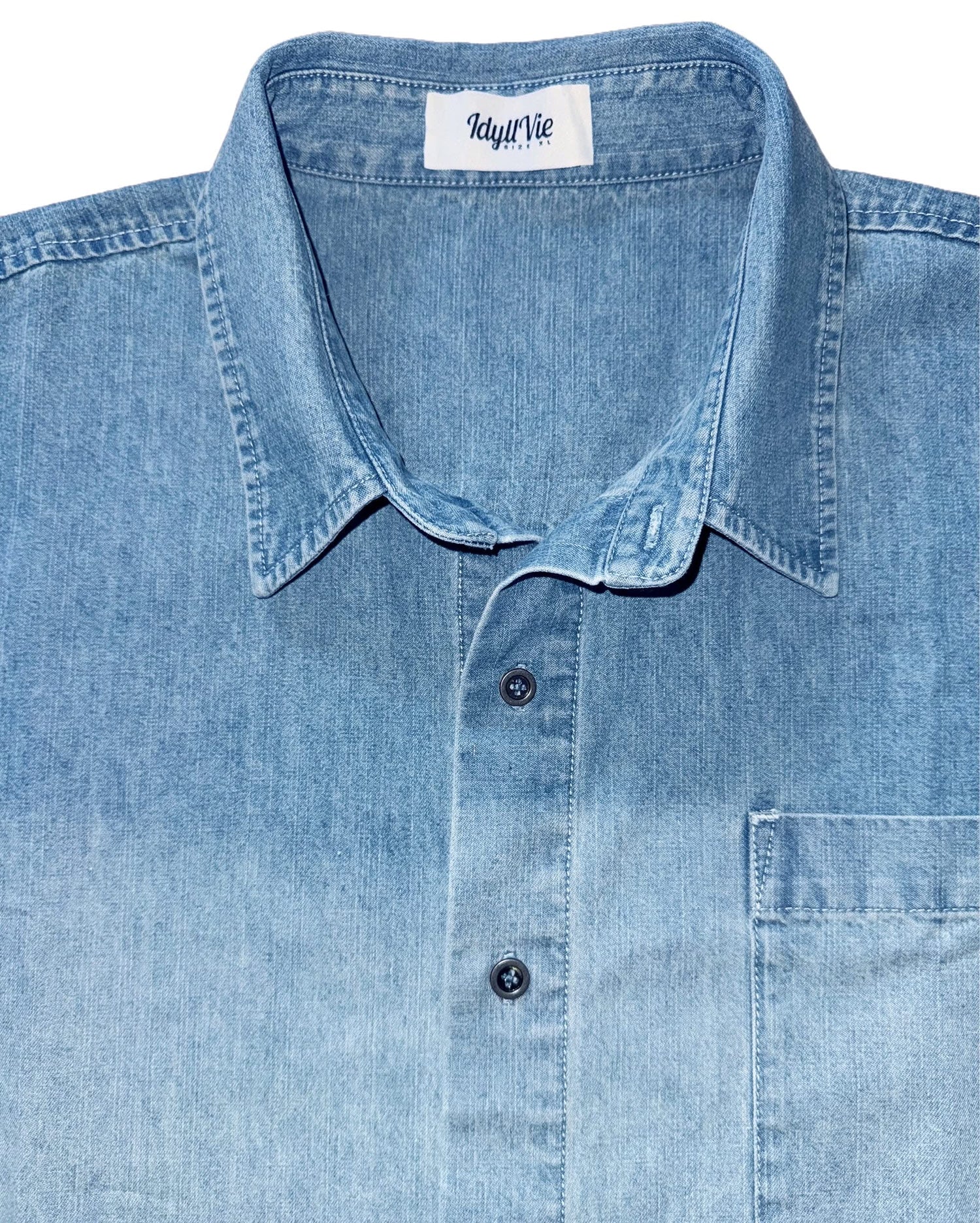 Close-up of IdyllVie Denim Shirt collar and chest pocket, showing button details and soft faded blue cotton fabric texture.
