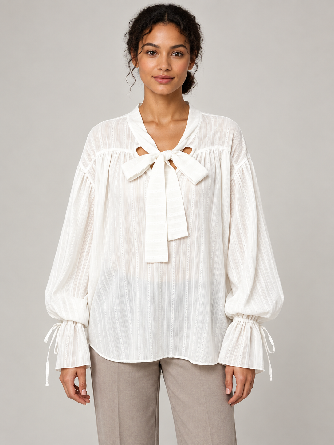 White textured tie-neck blouse with gathered tie cuffs, model front.