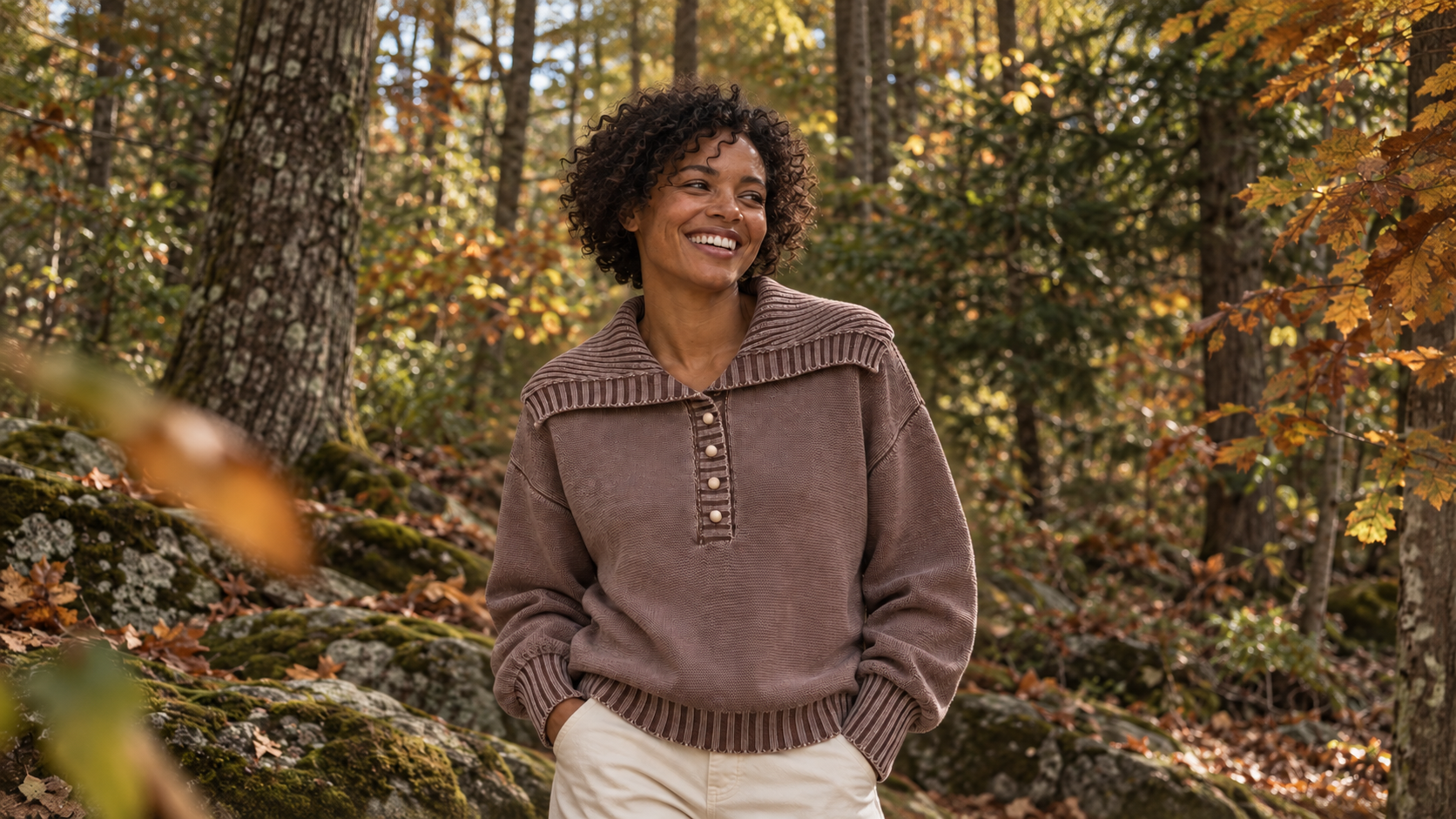 Woman wearing a brown polo sweater outdoors among autumn trees