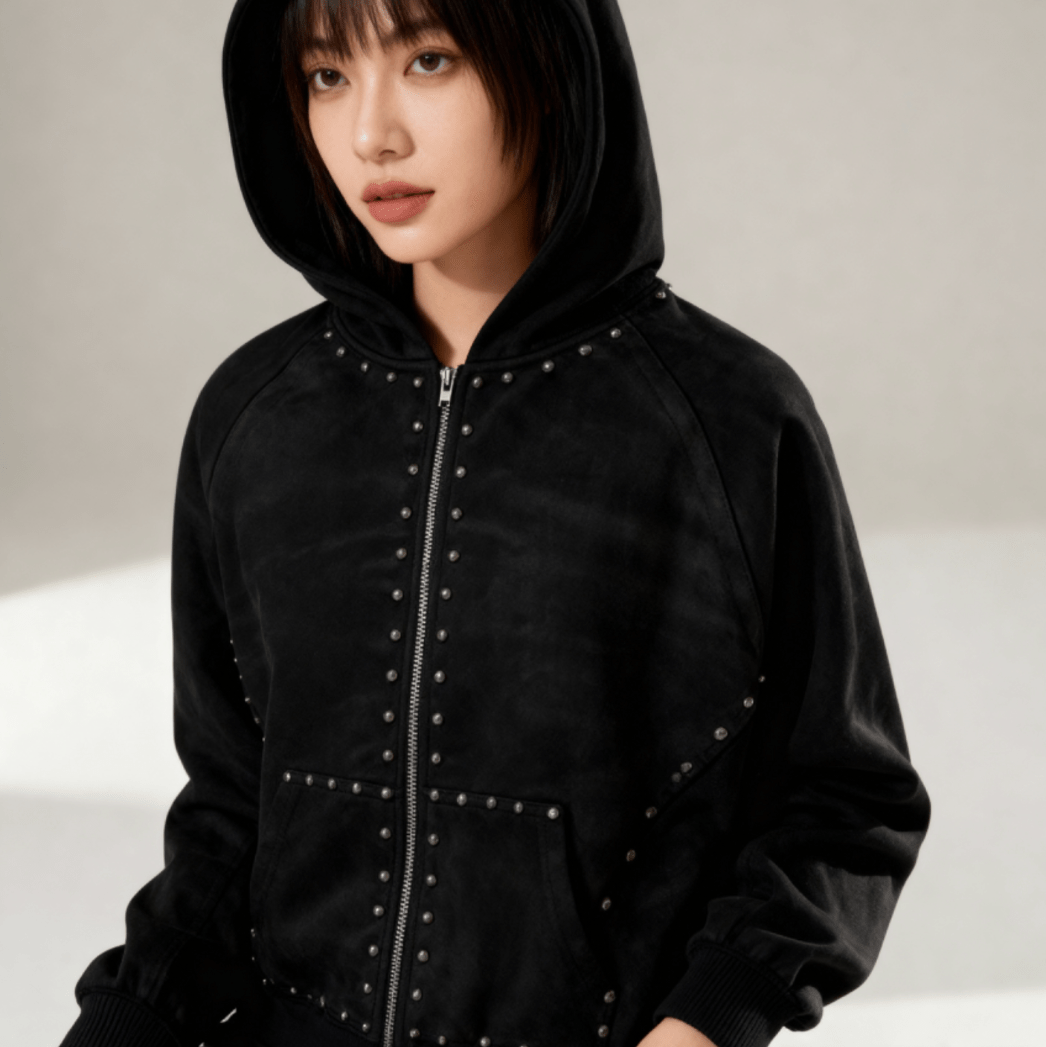 Female model in hooded black zip-up hoodie with studded detailing. Vintage-inspired design made from 100% cotton for comfort and style.