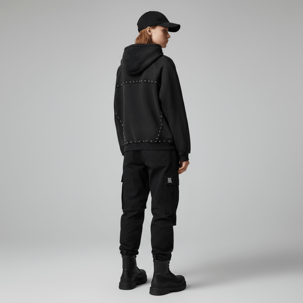 Rear view of female model in black studded zip-up hoodie. Features vintage-style stud accents and a modern streetwear silhouette.