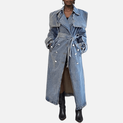 Model wearing a mid-length denim trench coat styled with a belted waist, double-breasted buttons, and classic lapel.