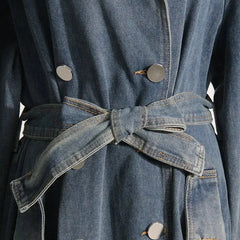 Detailed view of the belted waist and double-breasted buttons on a mid-length denim trench coat, emphasizing its stylish design.