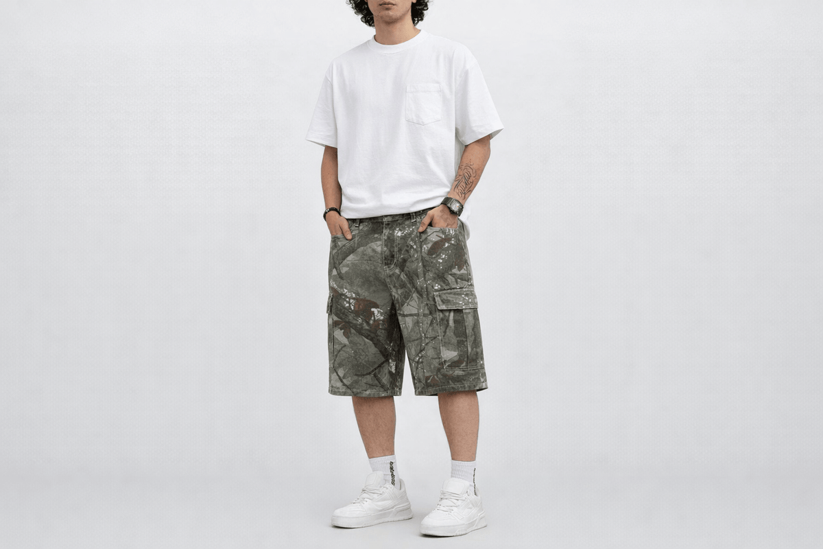 Model wearing green camo baggy jorts with a white T-shirt, front view