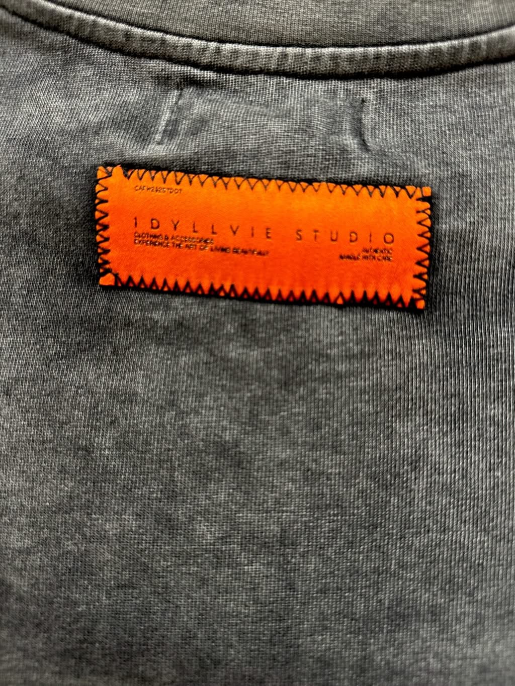 Macro shot of the orange IdyllVie Studio label stitched on the back of the heavyweight cotton t-shirt, showcasing brand detail and fabric texture.