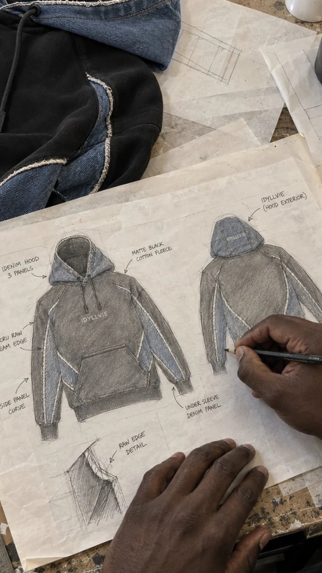 Hutton hoodie design sketches, denim samples and hands at the studio worktable.