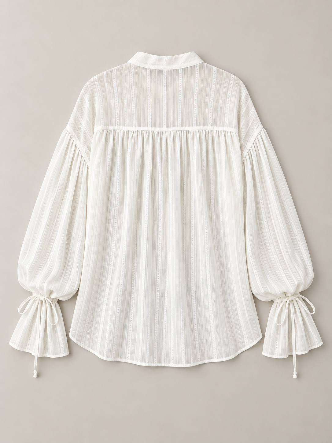 White textured tie-neck blouse with gathered tie cuffs, flat lay back.