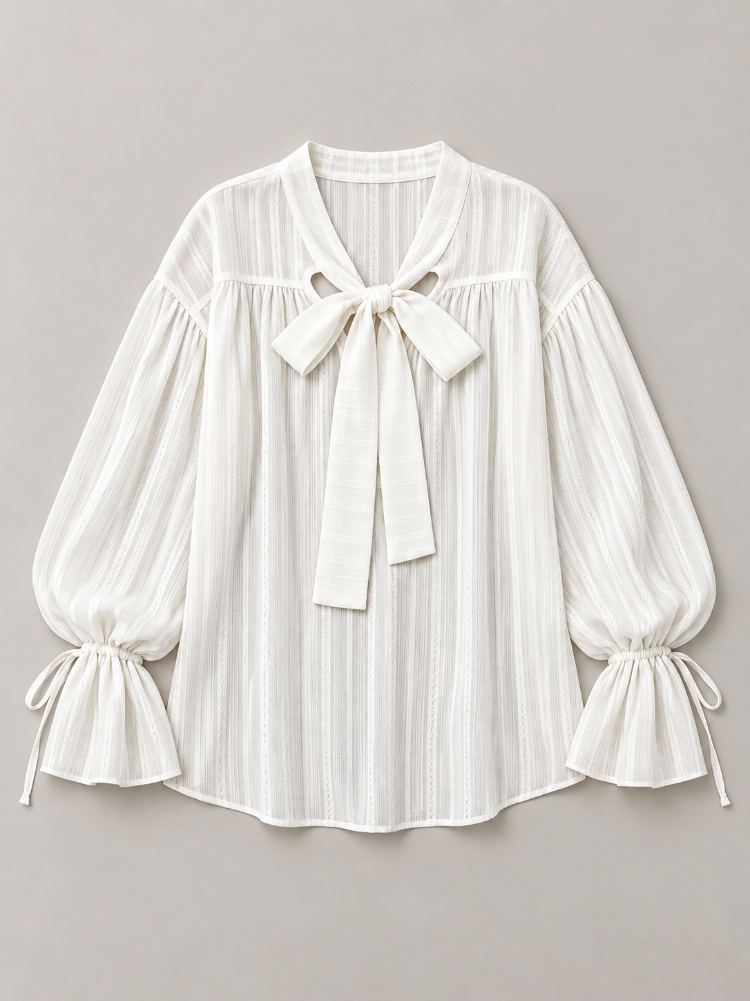 White textured tie-neck blouse with gathered tie cuffs, flat lay front.