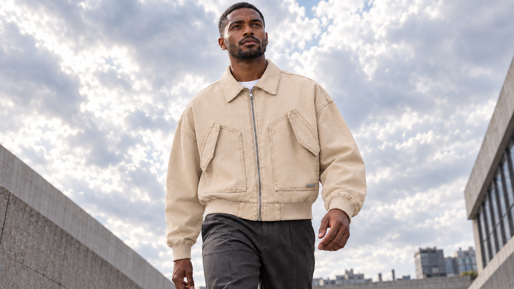 Man wearing a khaki cropped utility bomber beneath an overcast sky